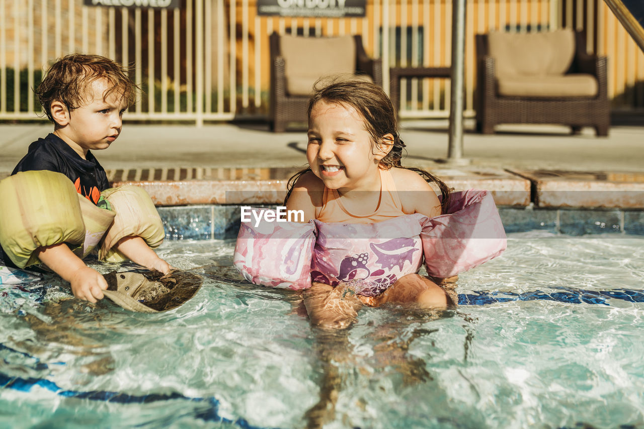 Front view of young siblings playing in pool on vacation in california