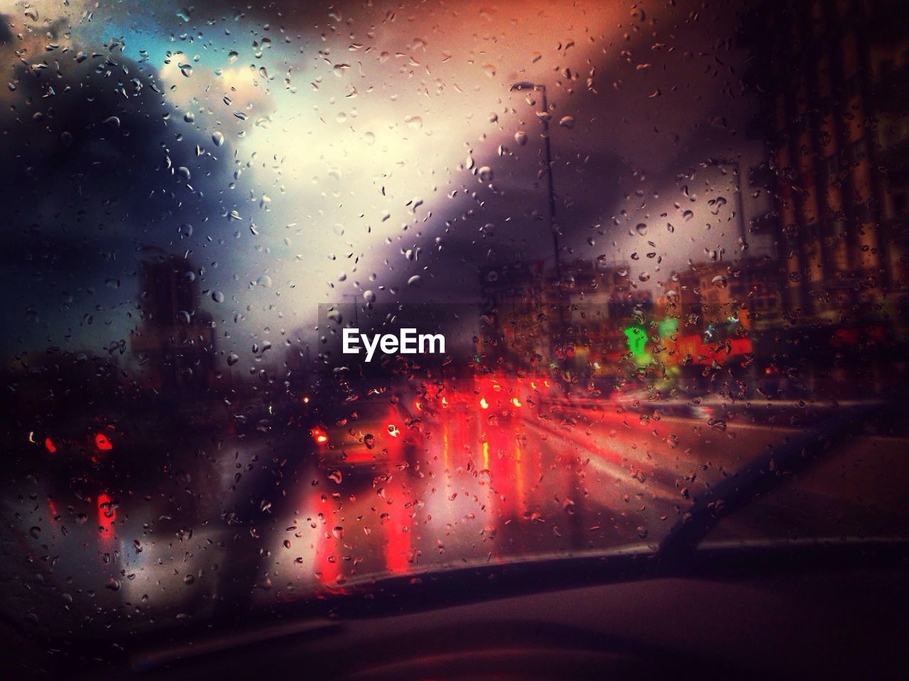 View of illuminated city street through wet car windshield