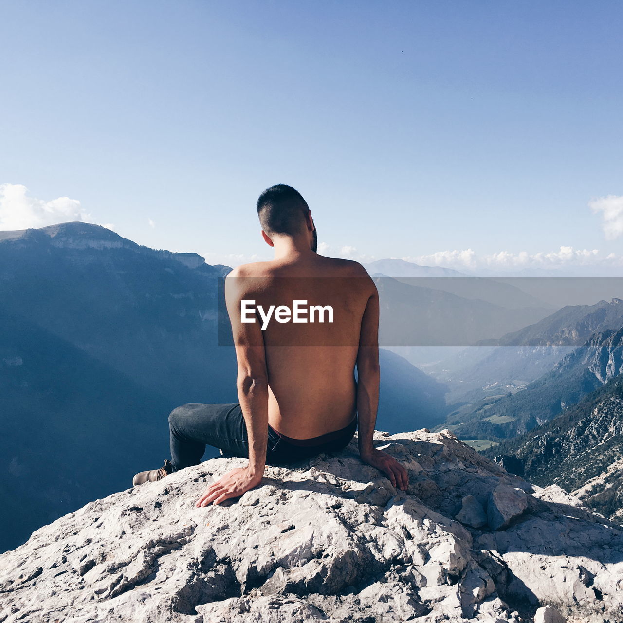 Rear view of shirtless man looking at mountains against sky