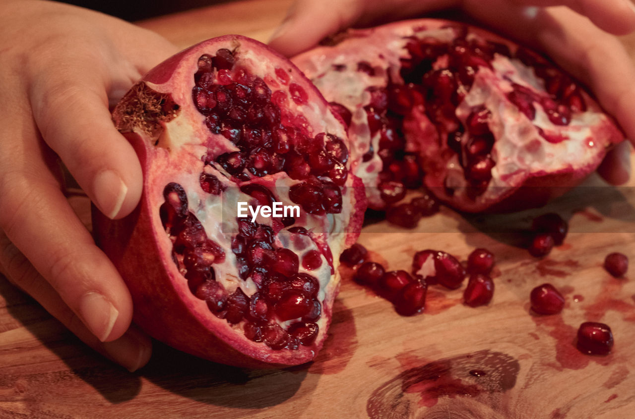 food and drink, food, pomegranate, hand, seed, freshness, plant, fruit, cross section, healthy eating, red, produce, pomegranate seed, wellbeing, indoors, cutting, slice, one person, cutting board, holding, adult, close-up, kitchen knife, juicy