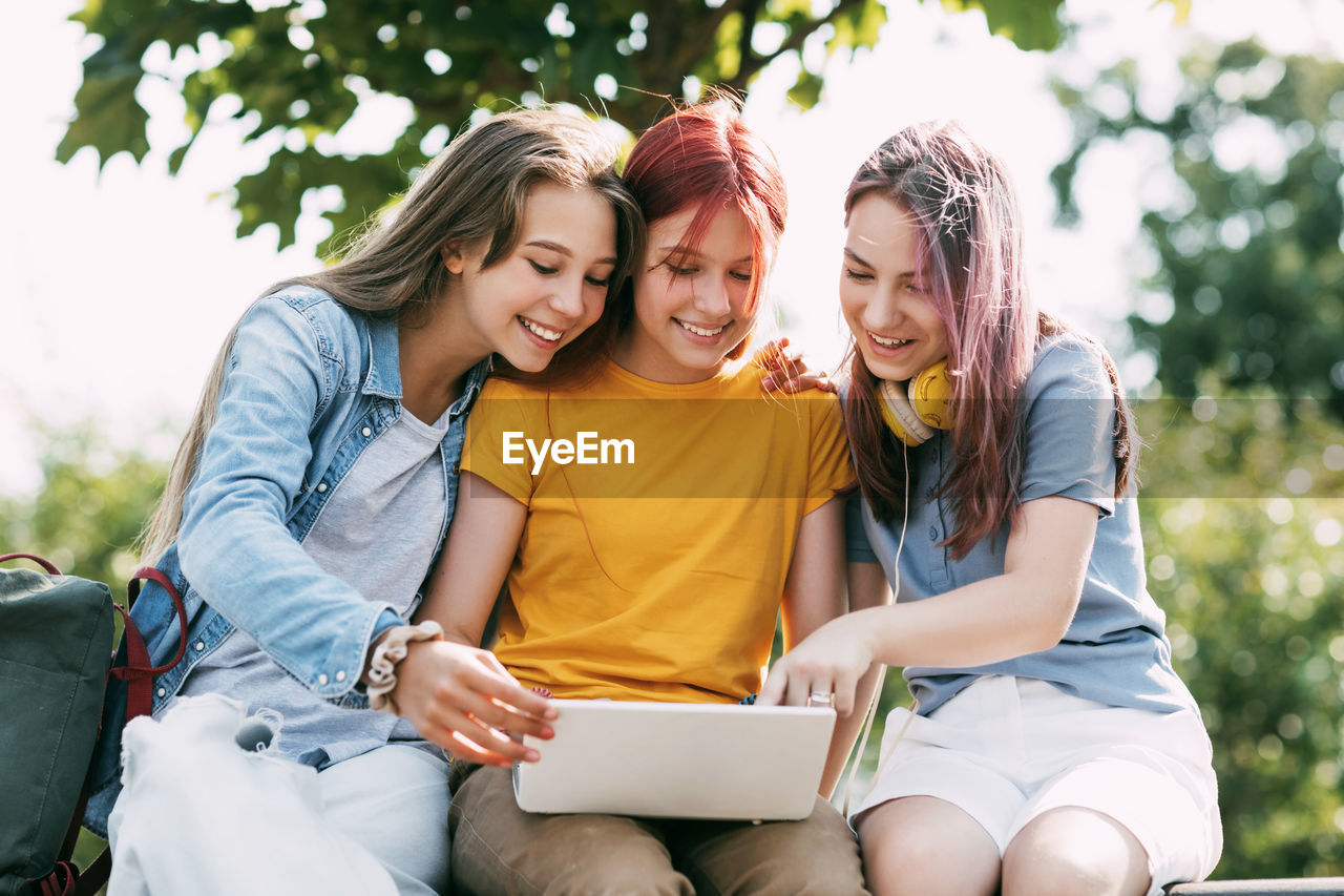 Three teenage girls communicate with their friends and classmates via video link using a laptop 