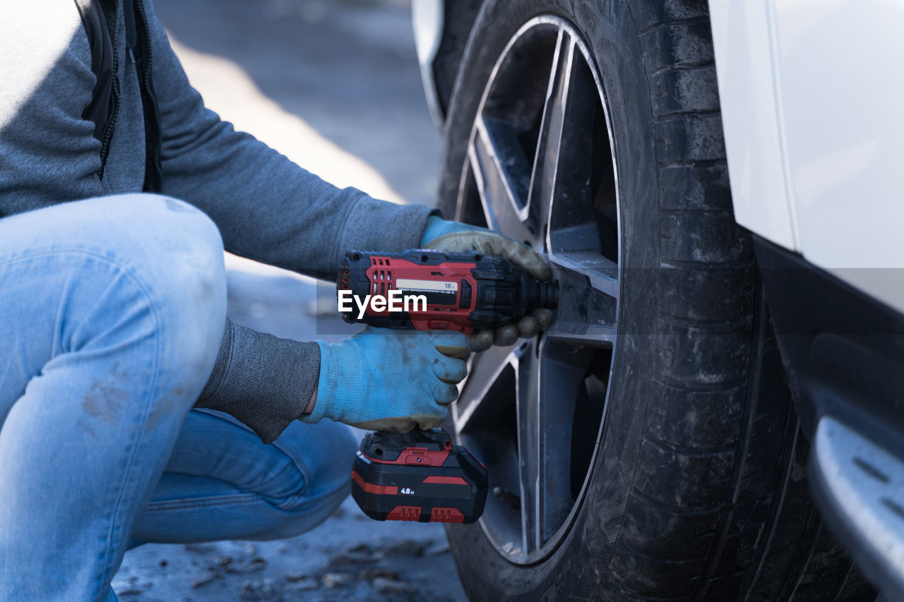 A man changes a wheel on a car, a seasonal change of rubber on a car