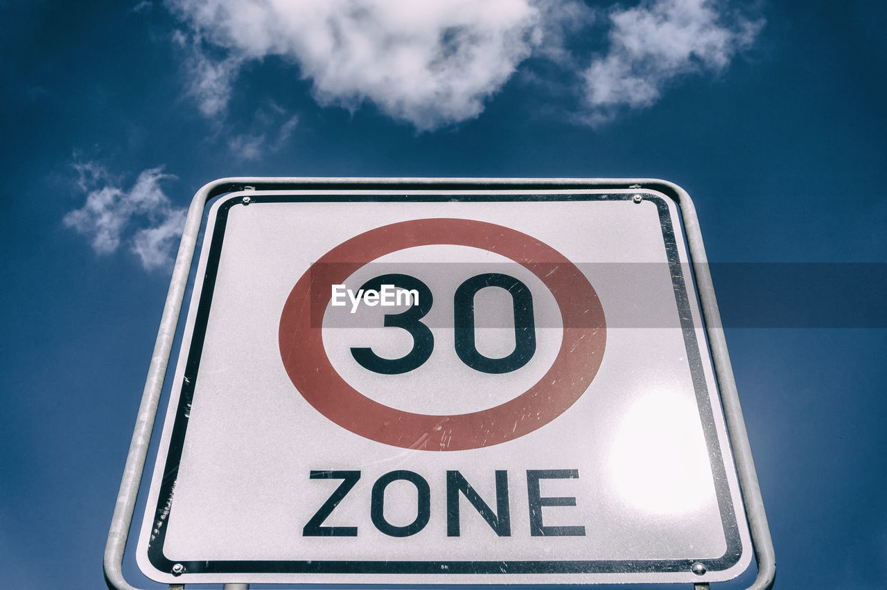 Low angle view of speed limit sign against blue sky during sunny day
