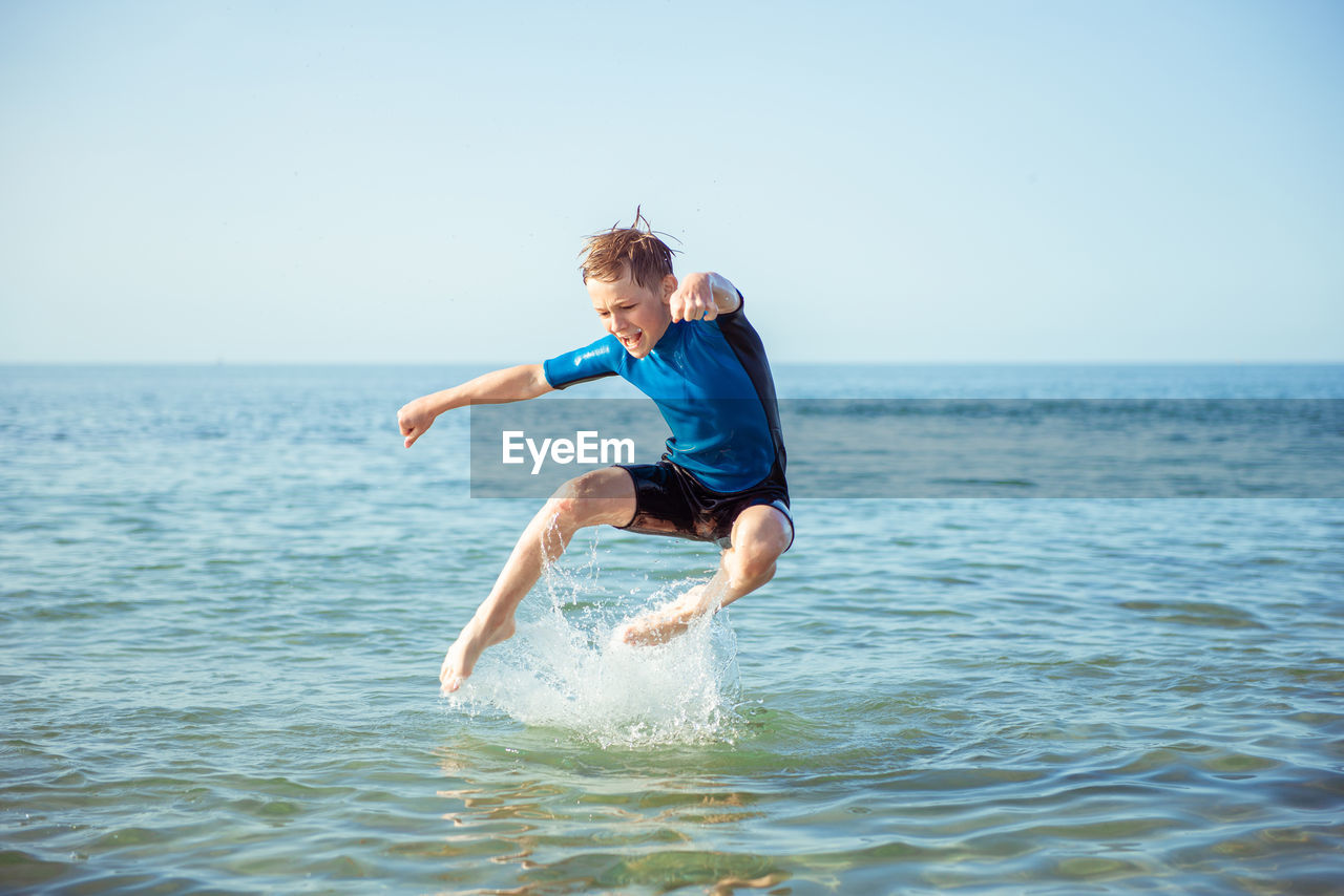Full length of boy jumping in sea water against sky
