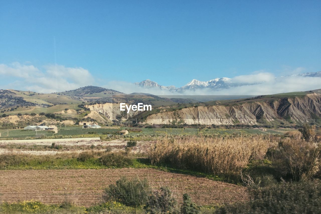 Scenic view of landscape and rocky mountains against clear blue sky on sunny day