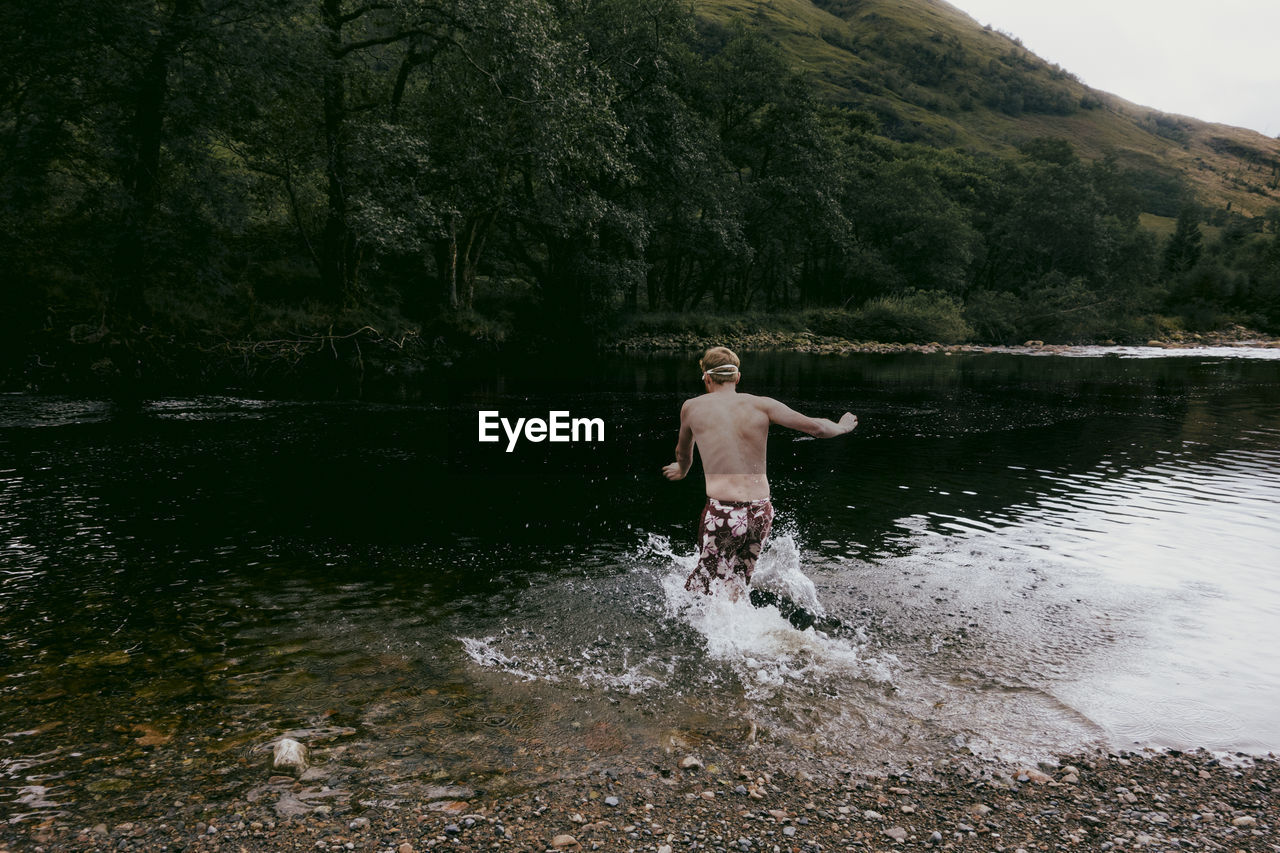 Shirtless man wading in lake