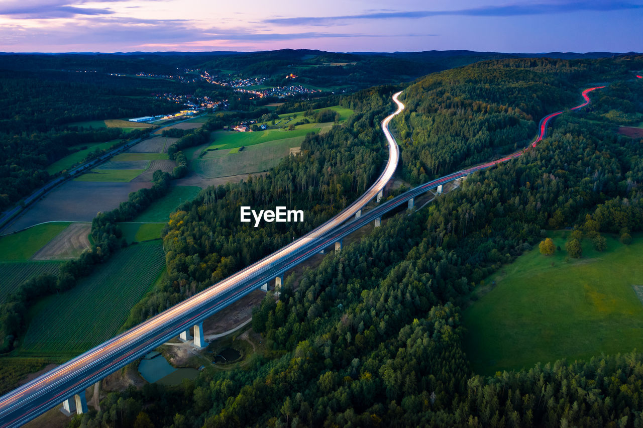 Aerial view of highway splitting aound forest hill on autumn evening