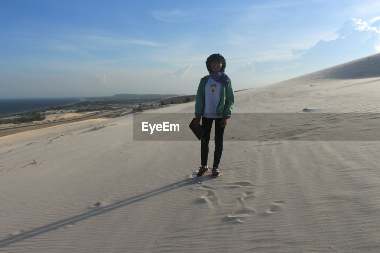 Young woman standing on sand against sky