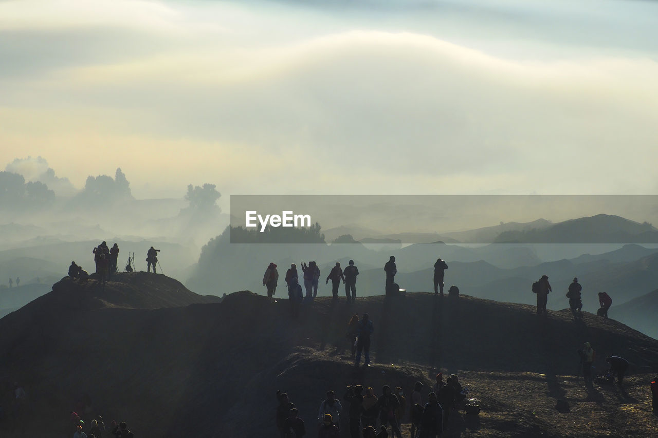 Silhouette people standing on mountain peak during foggy weather