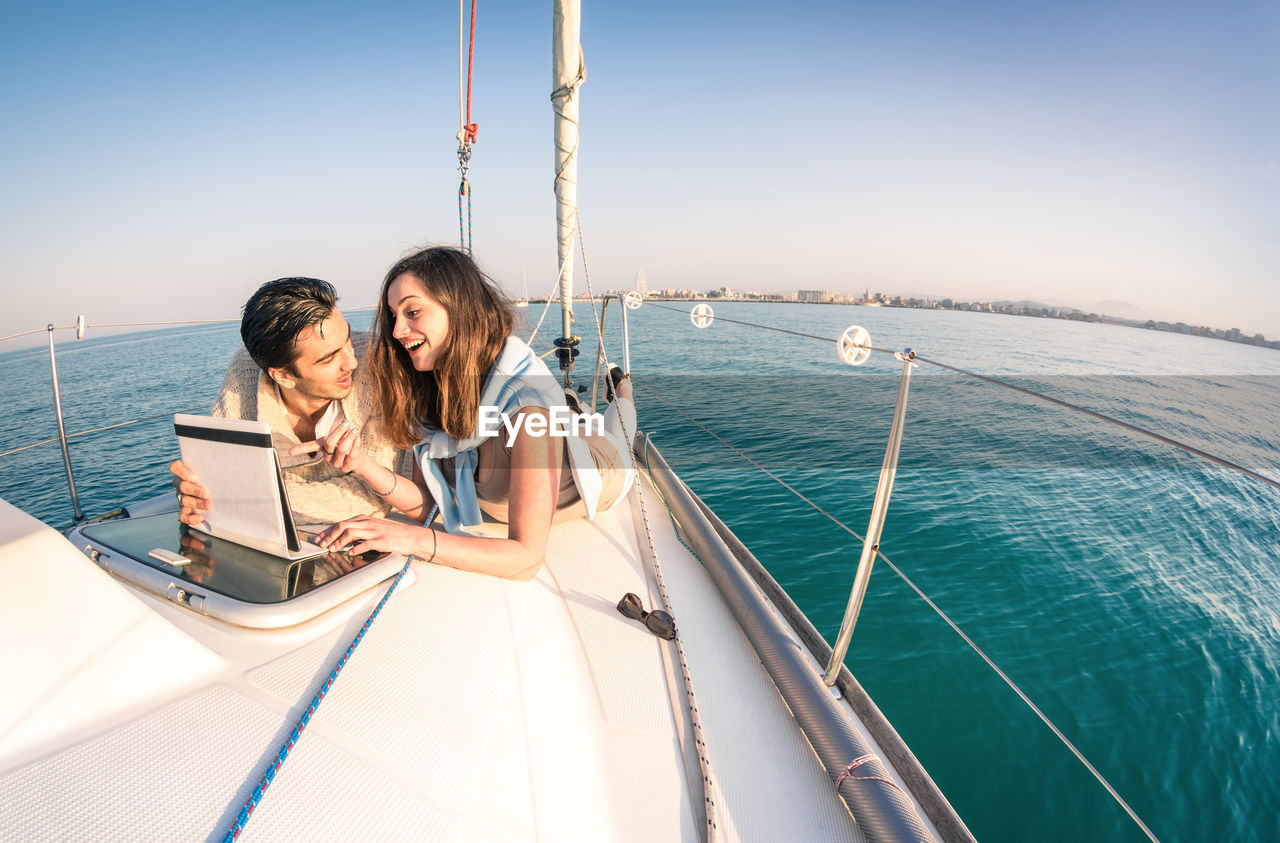 Couple lying on boat in sea against clear sky during sunset