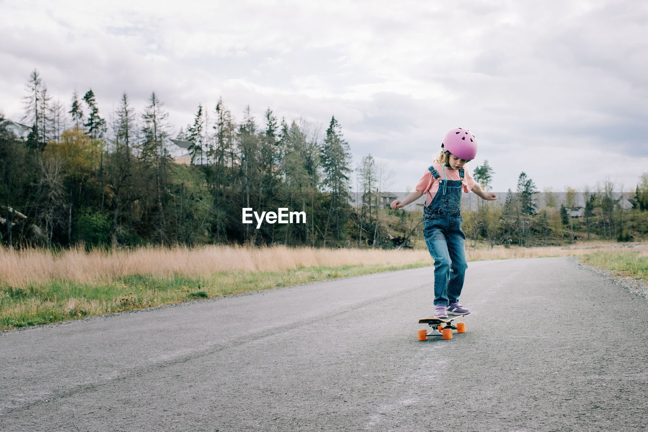 Young girl learning to skateboard on a country road