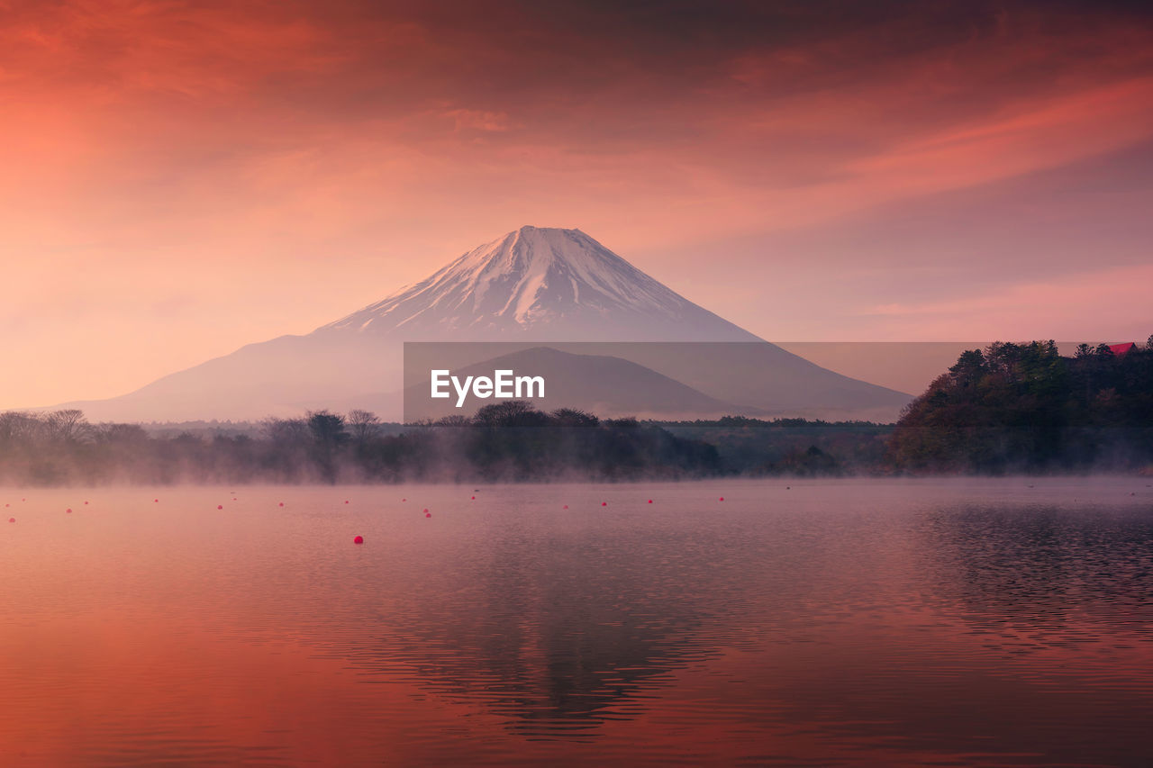 SCENIC VIEW OF LAKE BY MOUNTAINS AGAINST ORANGE SKY