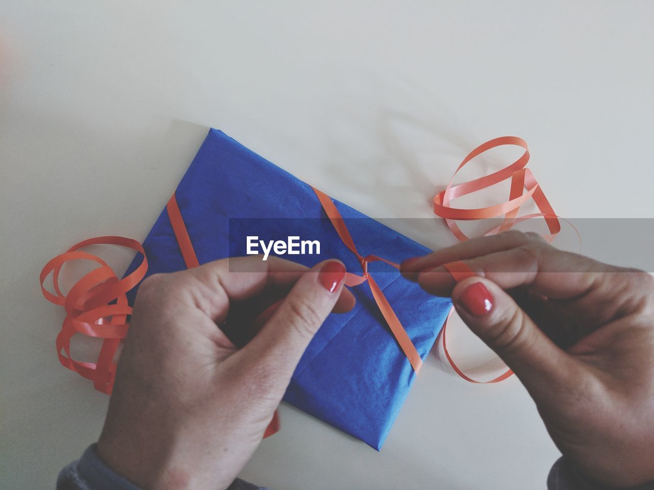 Cropped hands of woman tying ribbon on gift