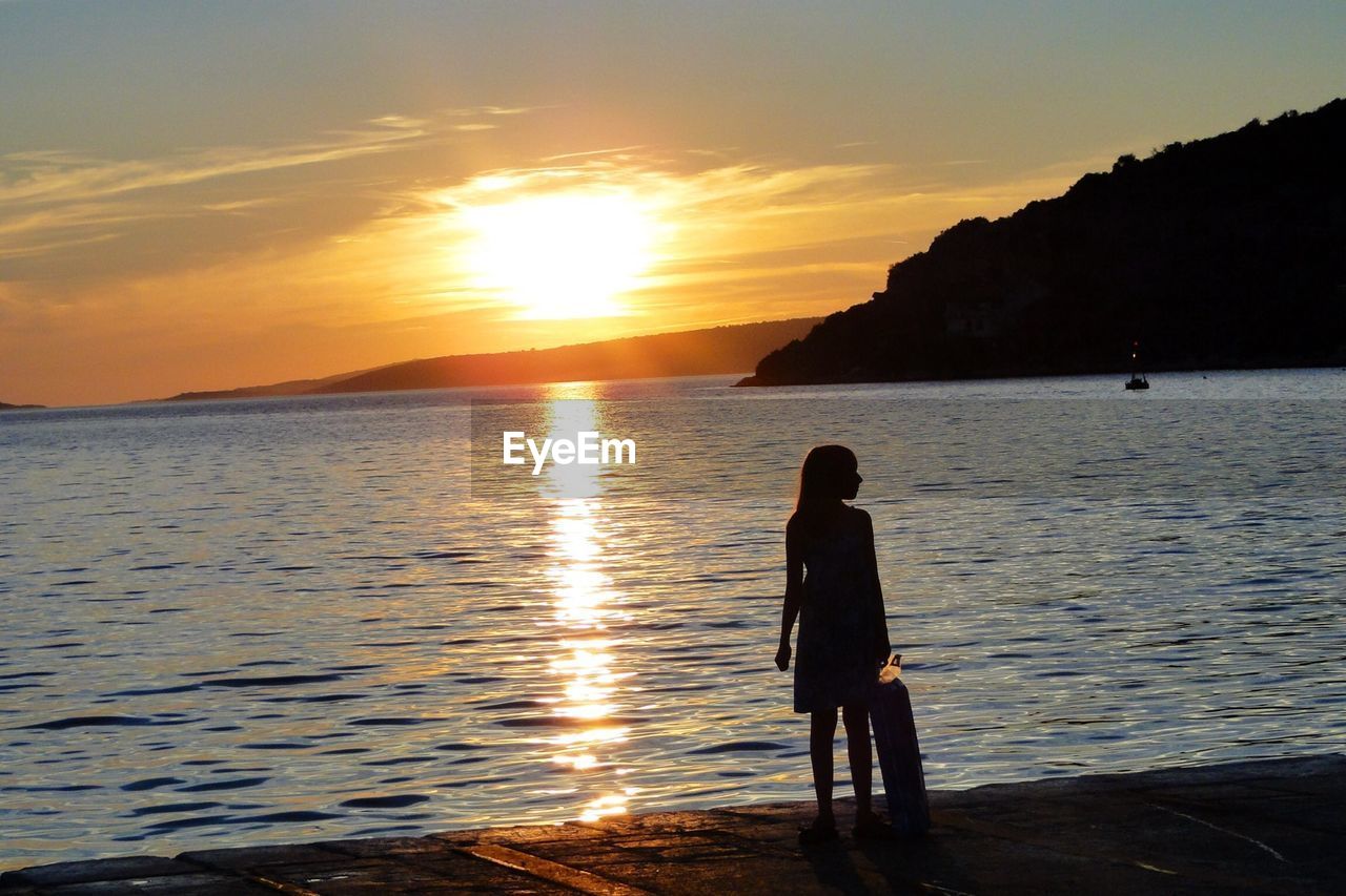 Rear view of silhouette woman standing at seaside during sunset