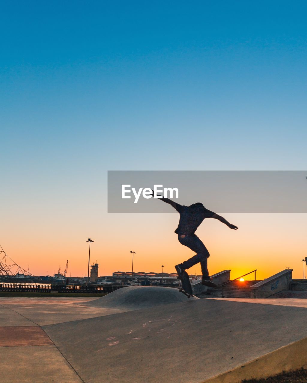 Rear view of man skateboarding on street against clear sky during sunset