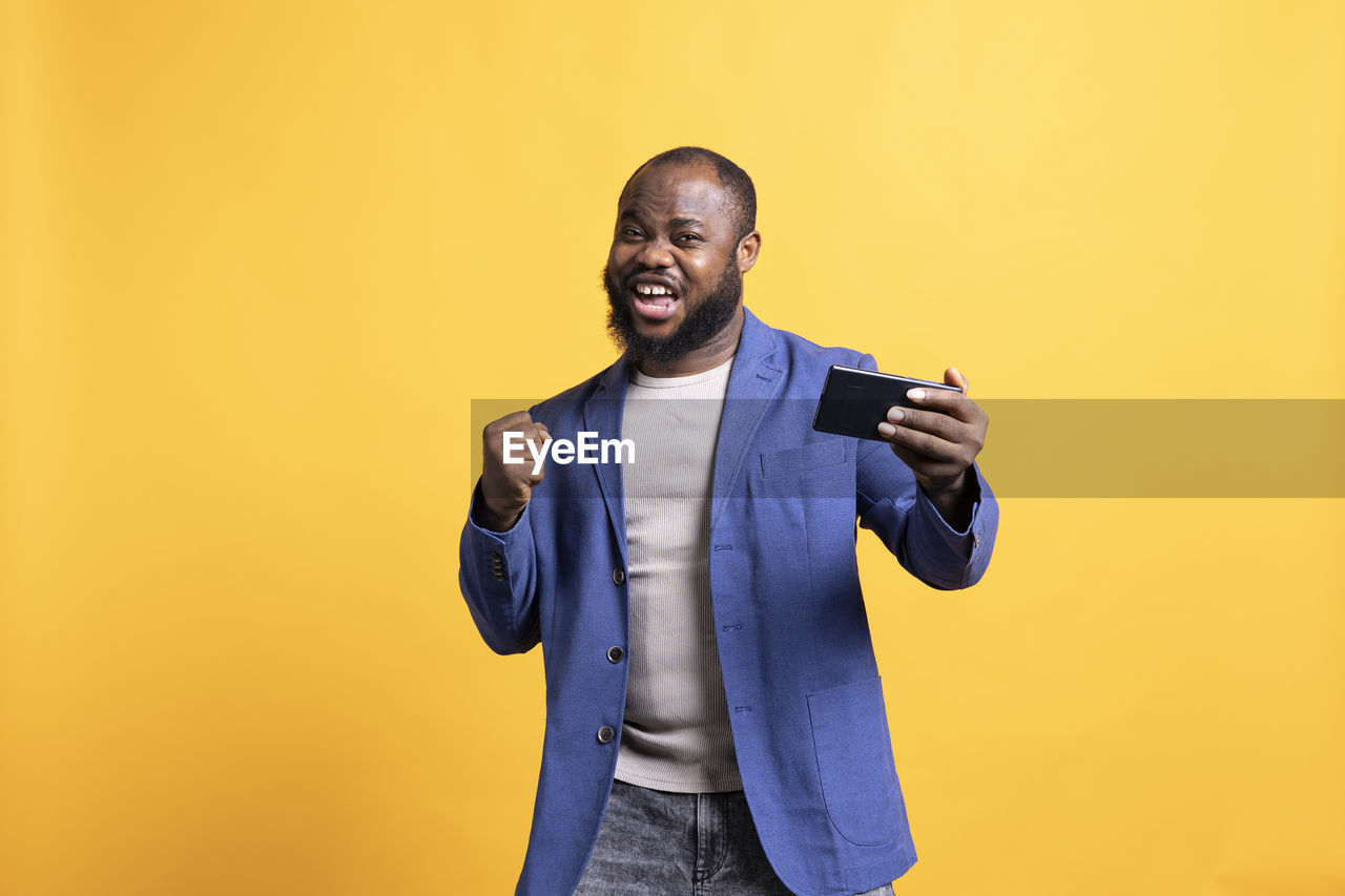 young man using mobile phone while standing against yellow background