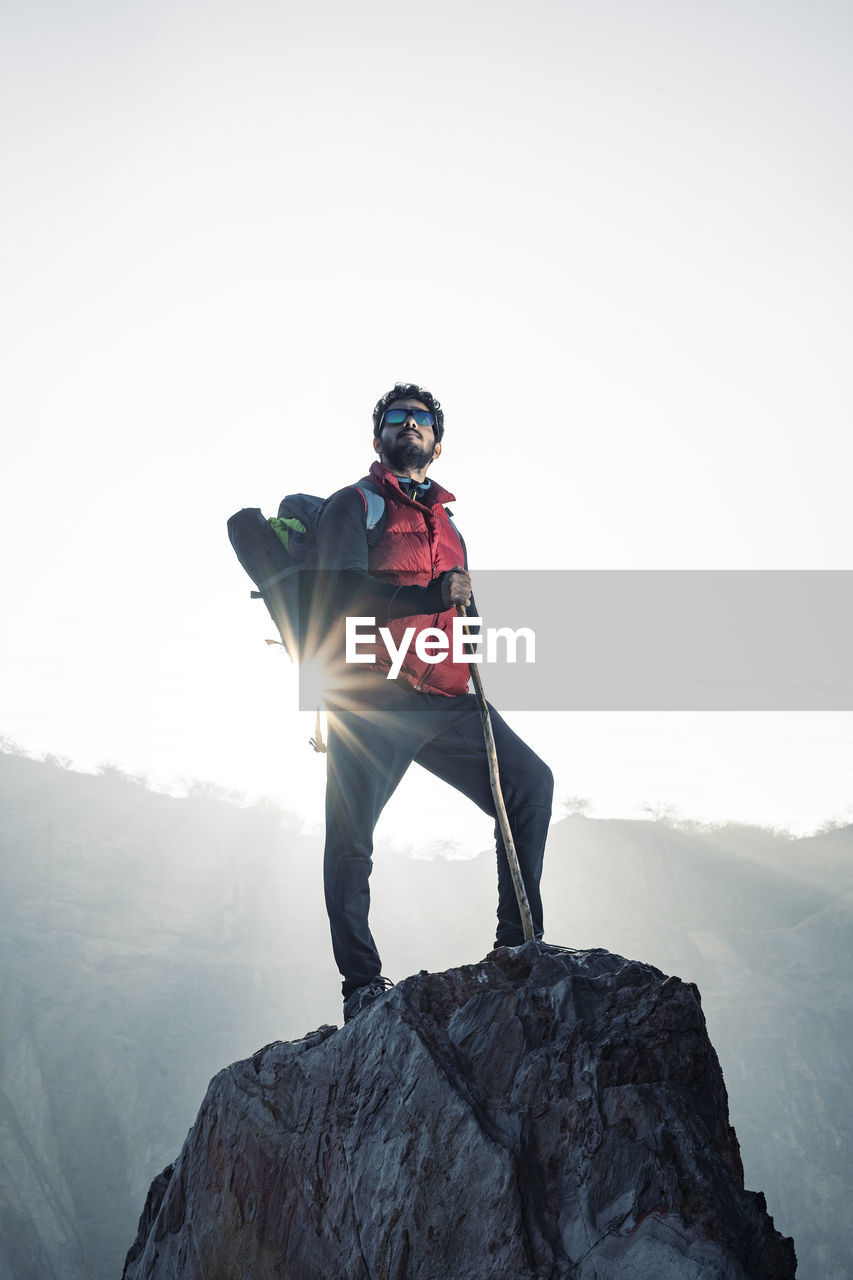 Young traveler in red snow jacket and a backpack standing on blue isolated background. 