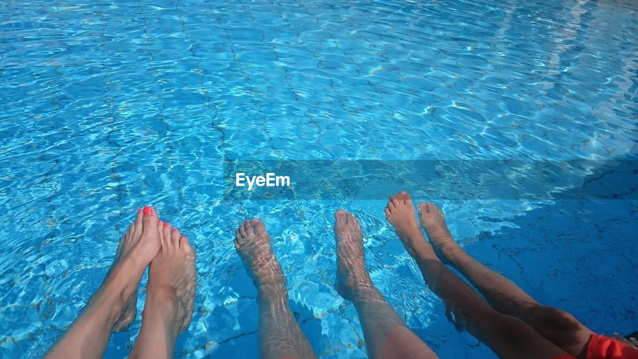 Low section of woman with kids in swimming pool during summer