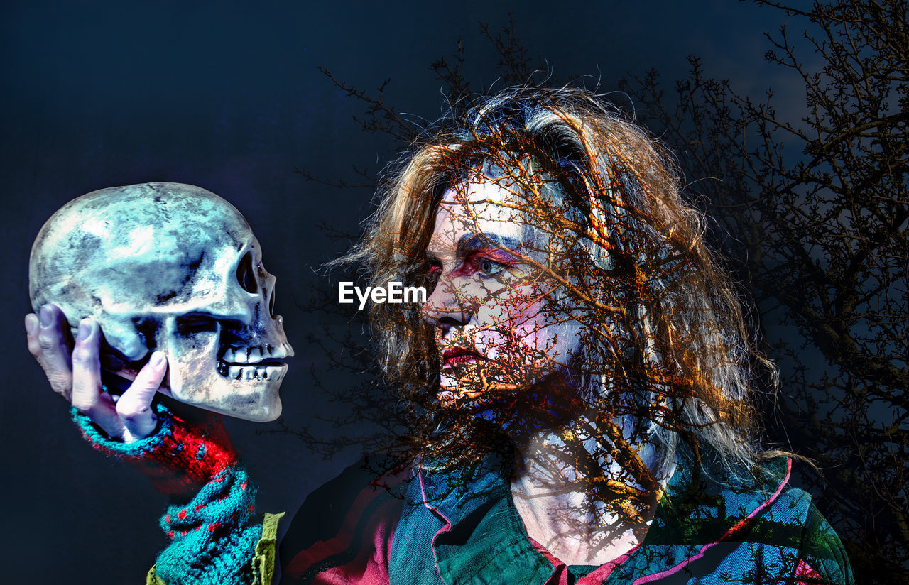 Multiple exposure of branches and spooky woman holding skull