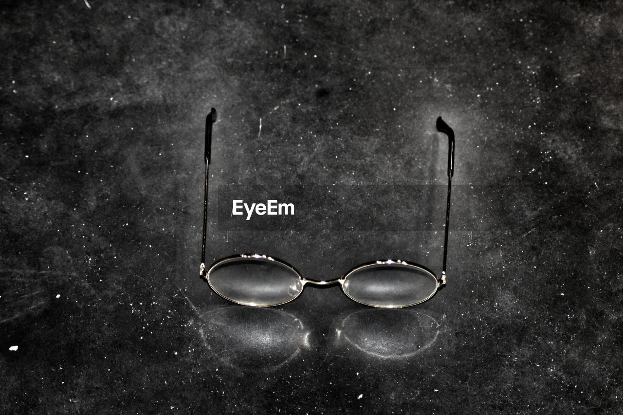 CLOSE-UP OF EYEGLASSES ON TABLE AGAINST BLACK BACKGROUND