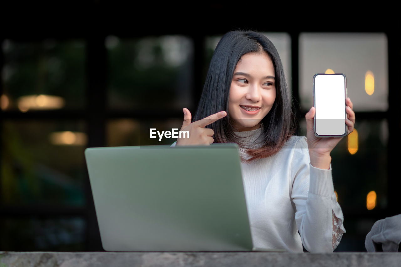 PORTRAIT OF A SMILING YOUNG WOMAN USING LAPTOP