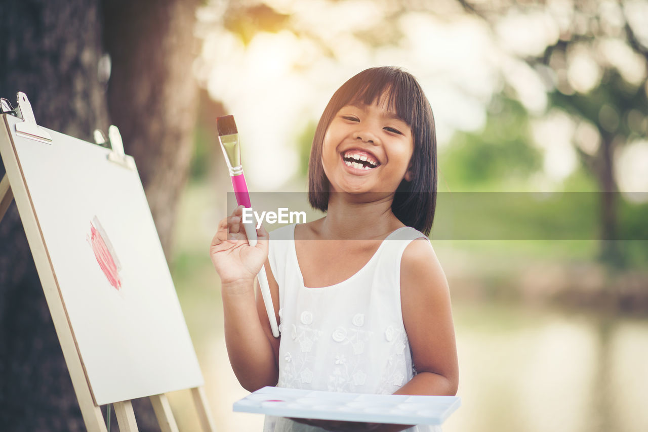 Portrait of happy girl painting on canvas