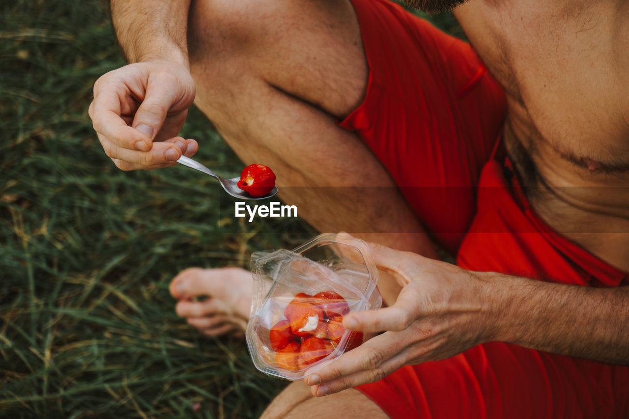 Low section of shirtless man having red fruits on field