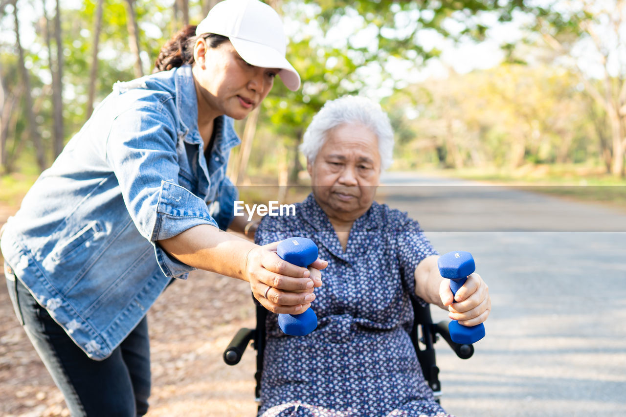 Woman assisting senior patient holding dumbbells