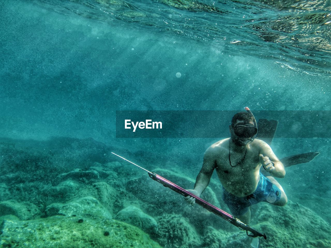 Shirtless man holding harpoon swimming undersea