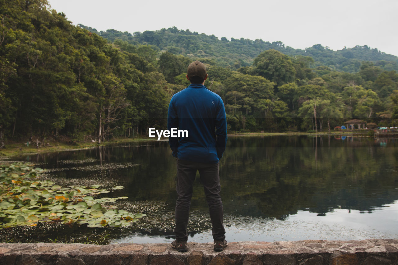 Rear view of man standing by lake against clear sky