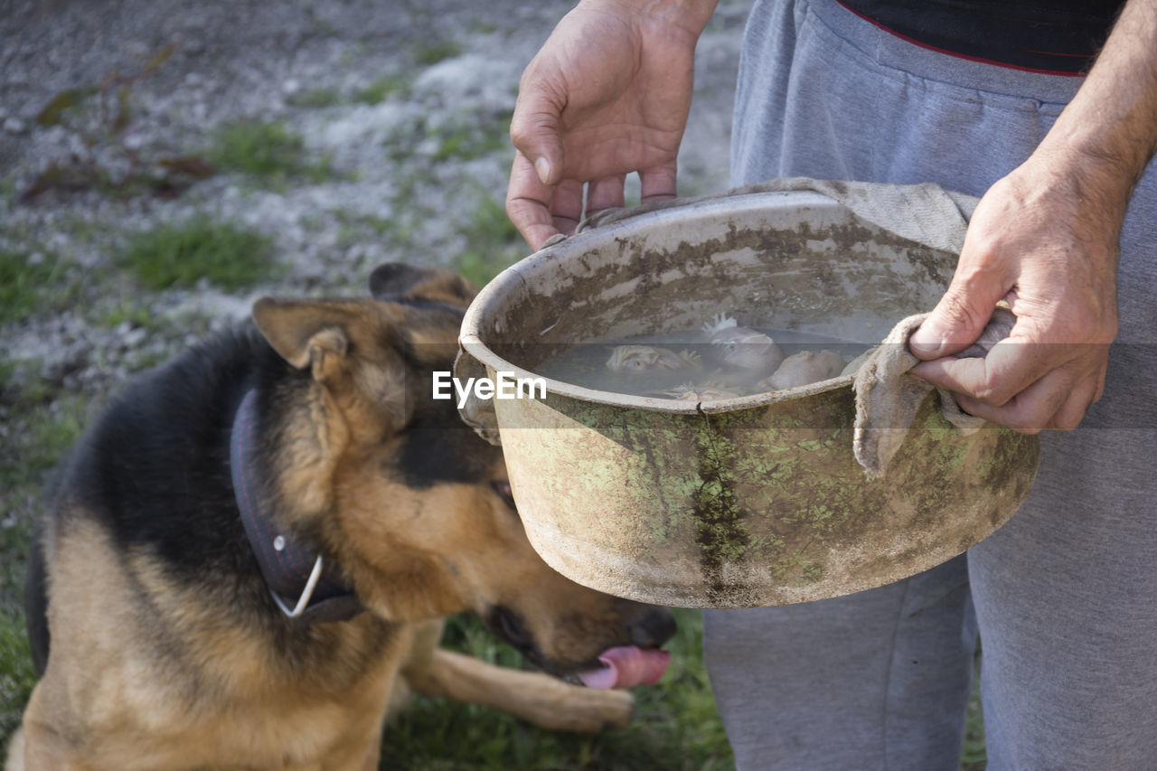 MIDSECTION OF MAN HOLDING DOG WHILE STANDING OUTDOORS