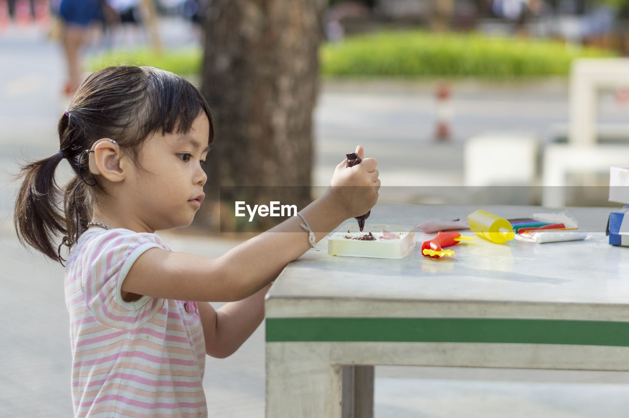 Side view of girl playing with watercolor paints on table