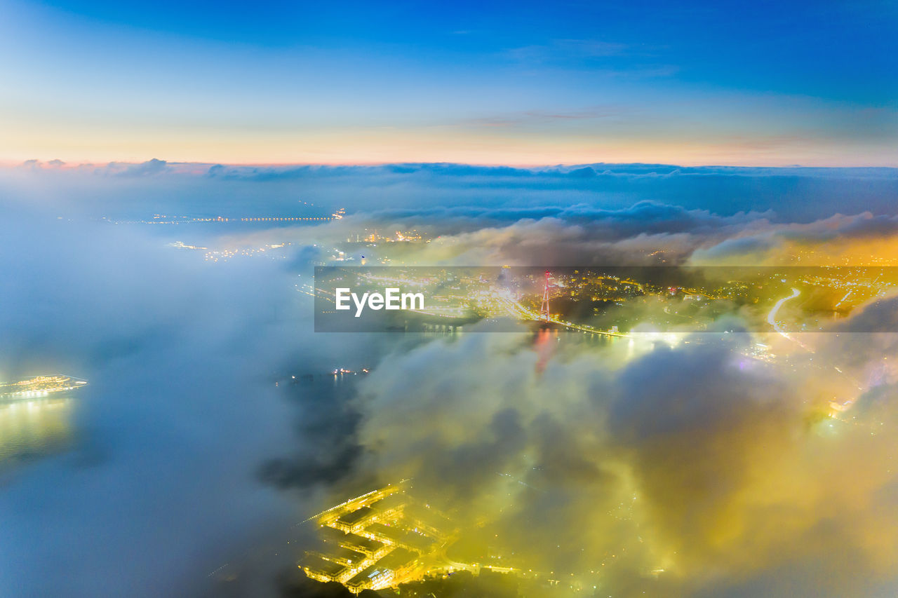 AERIAL VIEW OF ILLUMINATED CITY AGAINST SKY AT SUNSET