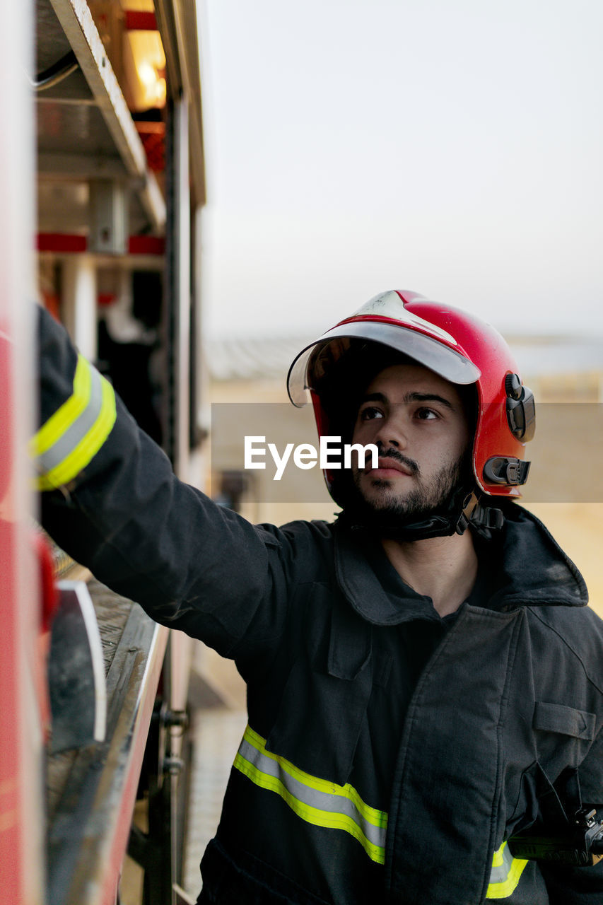 Tranquil worker wearing protective uniform and red hardhat operating inside fire truck