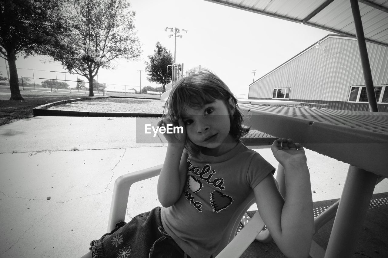 Portrait of girl sitting on chair at poolside