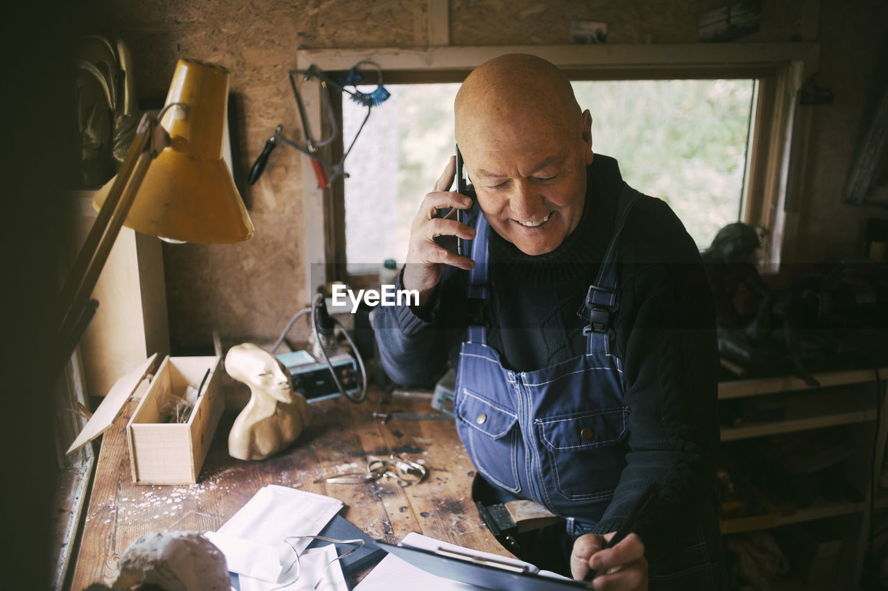 Smiling businessman talking on smart phone in workshop