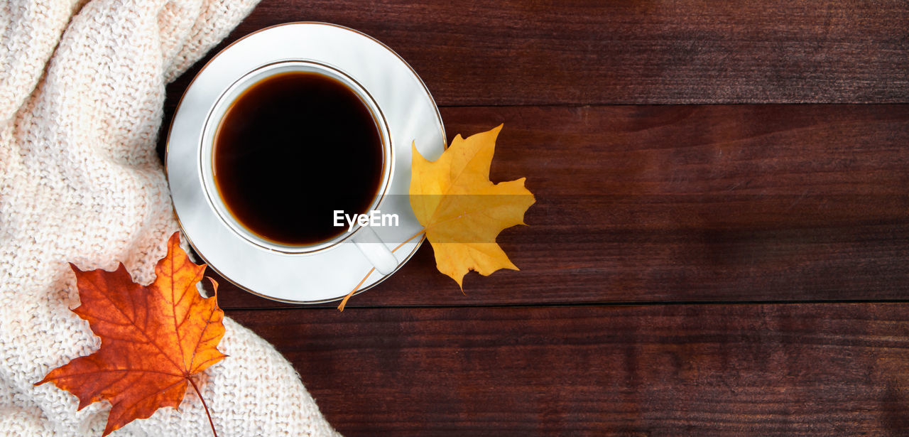 leaf, autumn, plant part, cup, mug, yellow, wood, food and drink, drink, refreshment, coffee, table, dry, maple leaf, directly above, orange color, no people, coffee cup, brown, hot drink, nature, high angle view, tea, still life, black coffee, indoors, flower, maple tree, close-up, food, copy space, freshness