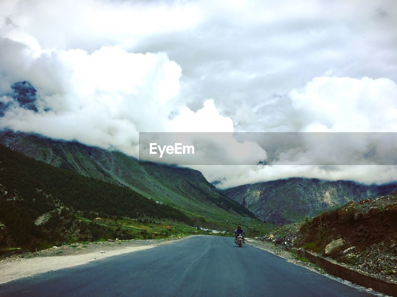 Man riding motorcycle on road amidst mountains against sky