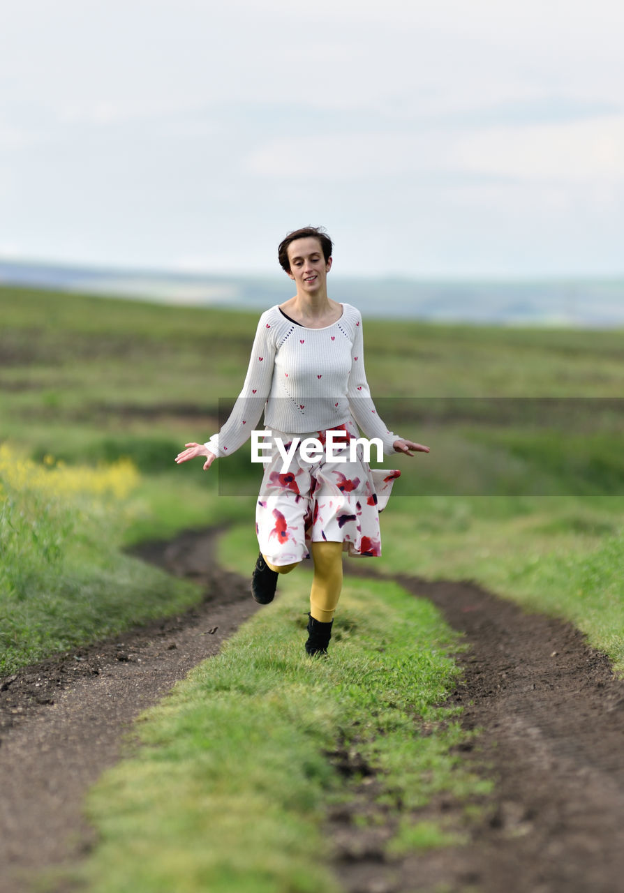 Joyful young woman in skirt running in canola field in the spring