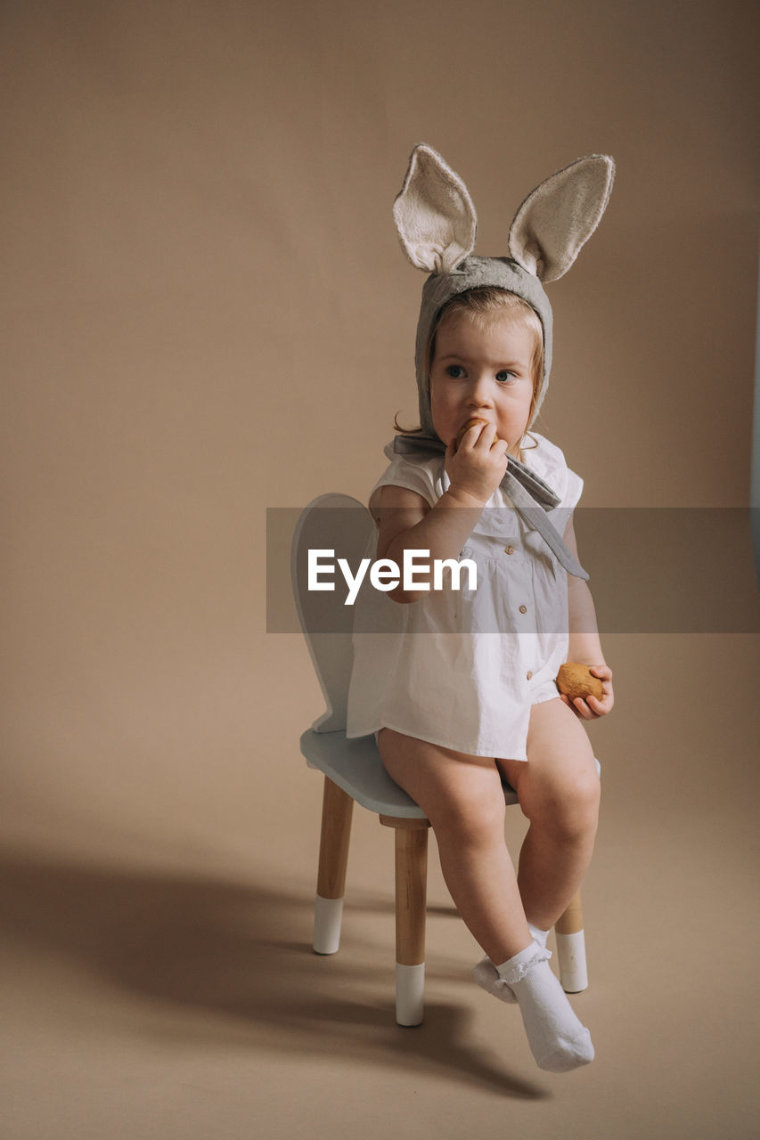 Toddler baby girl in funny hat with ears sitting with eggs in her hand