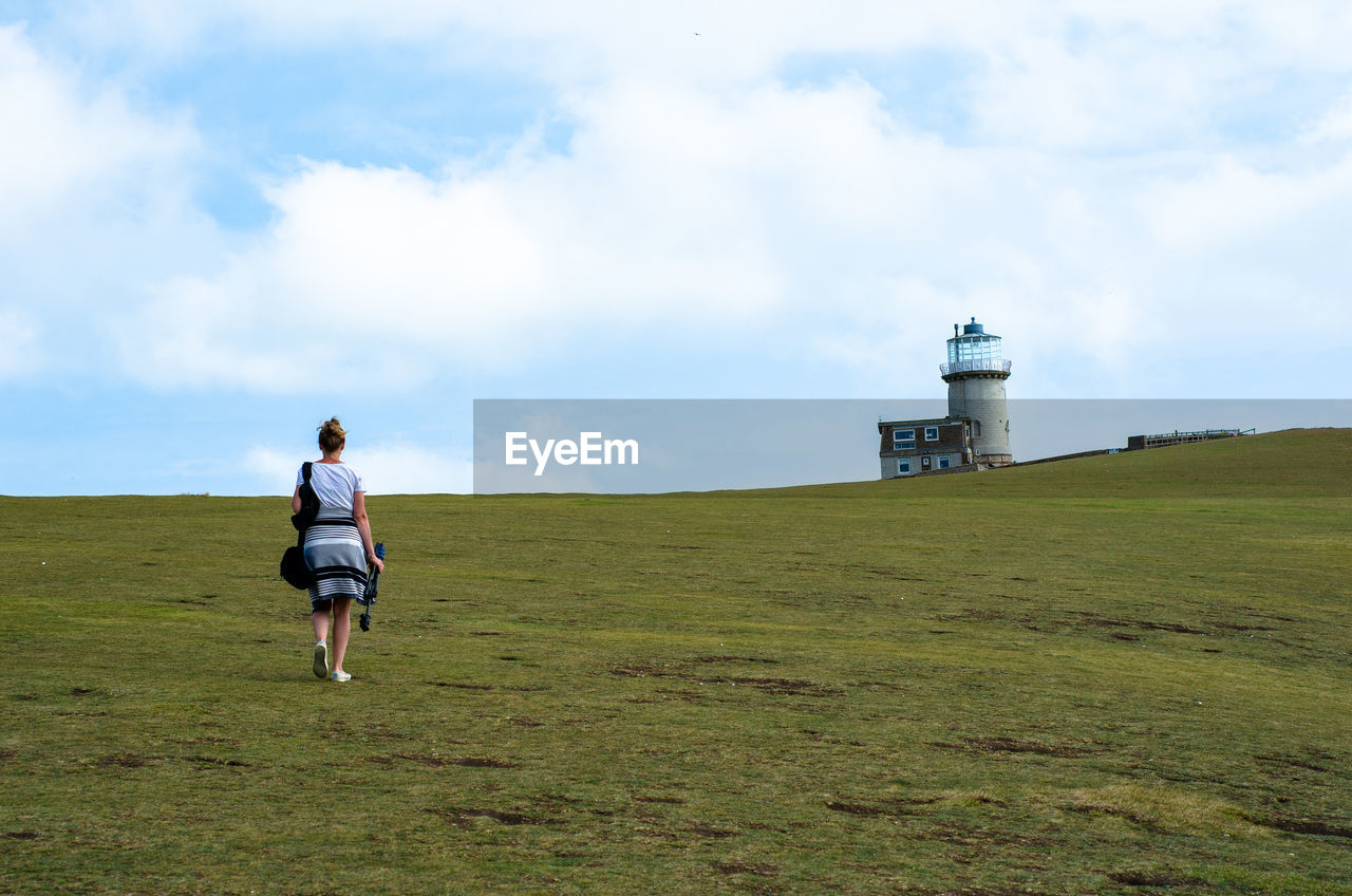 Rear view of woman walking on field against sky