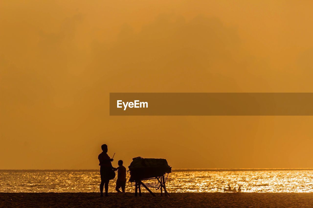 Silhouette people at beach against orange sky during sunset