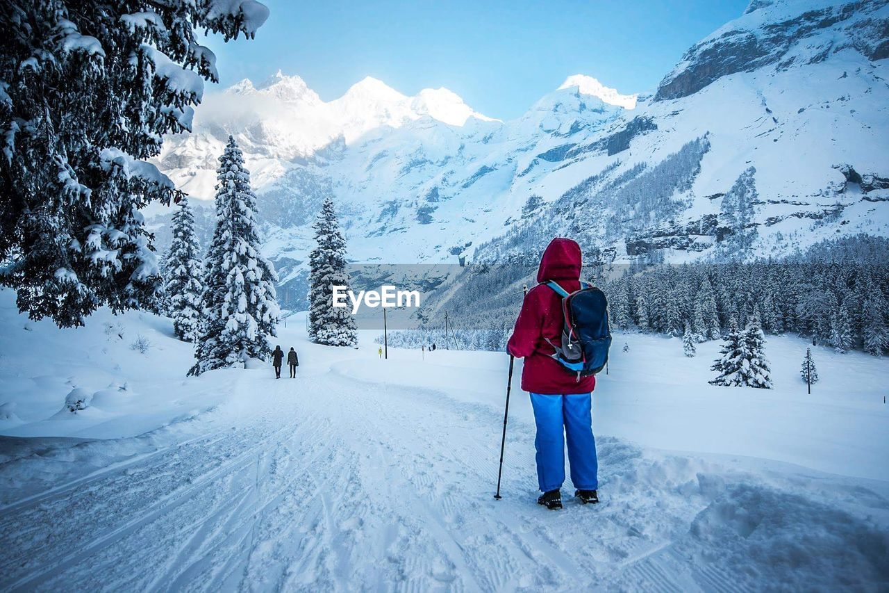 REAR VIEW OF MAN ON SNOWCAPPED MOUNTAIN