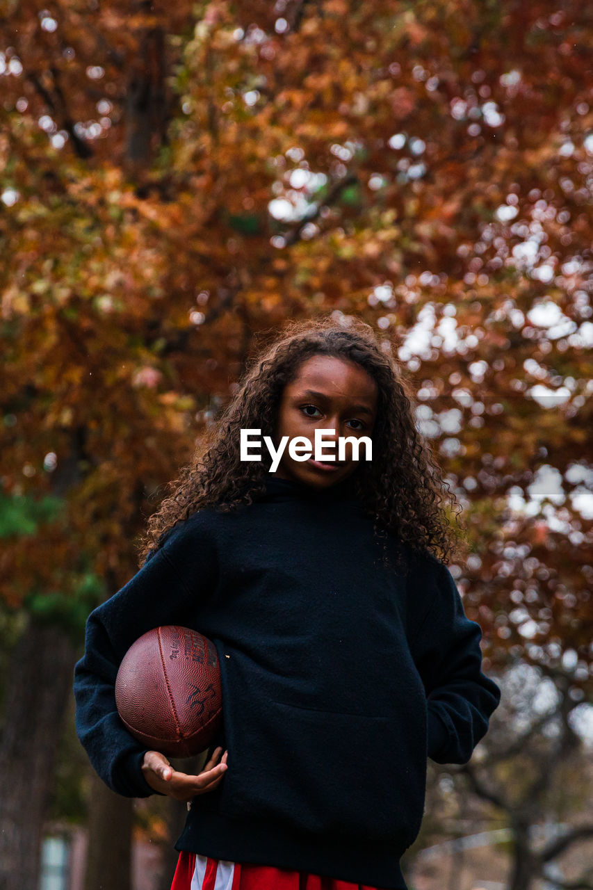 Portrait of confident girl holding american football in park