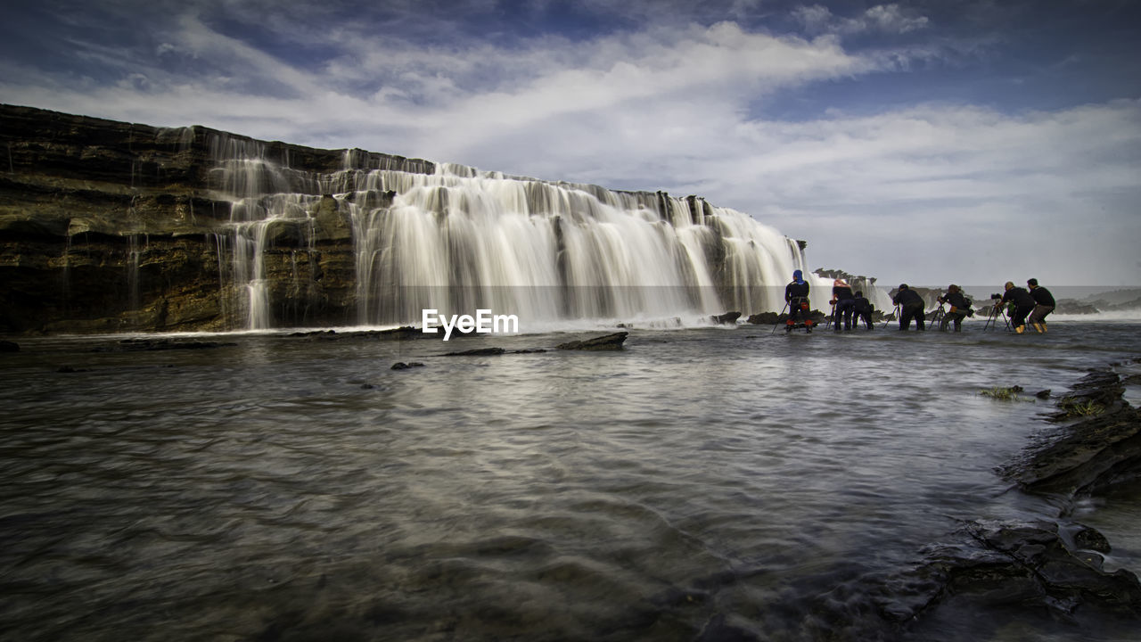 People photographing waterfall against sky