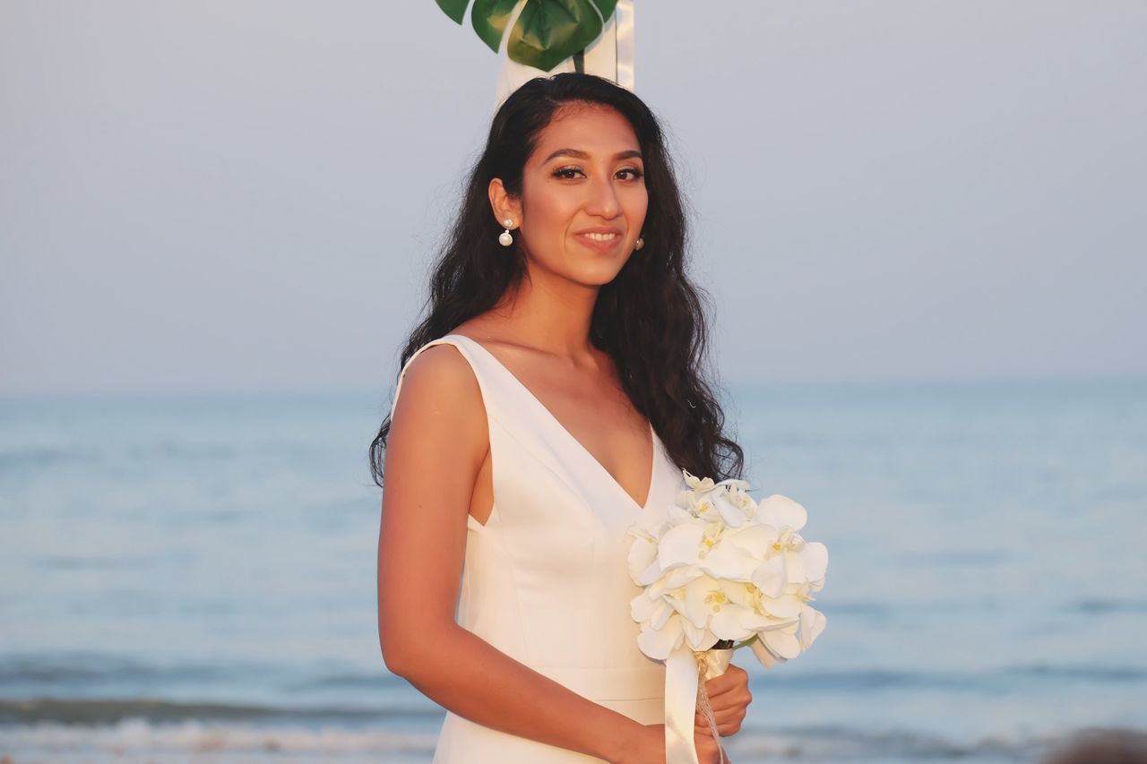 Portrait of woman with bouquet standing at beach against sky