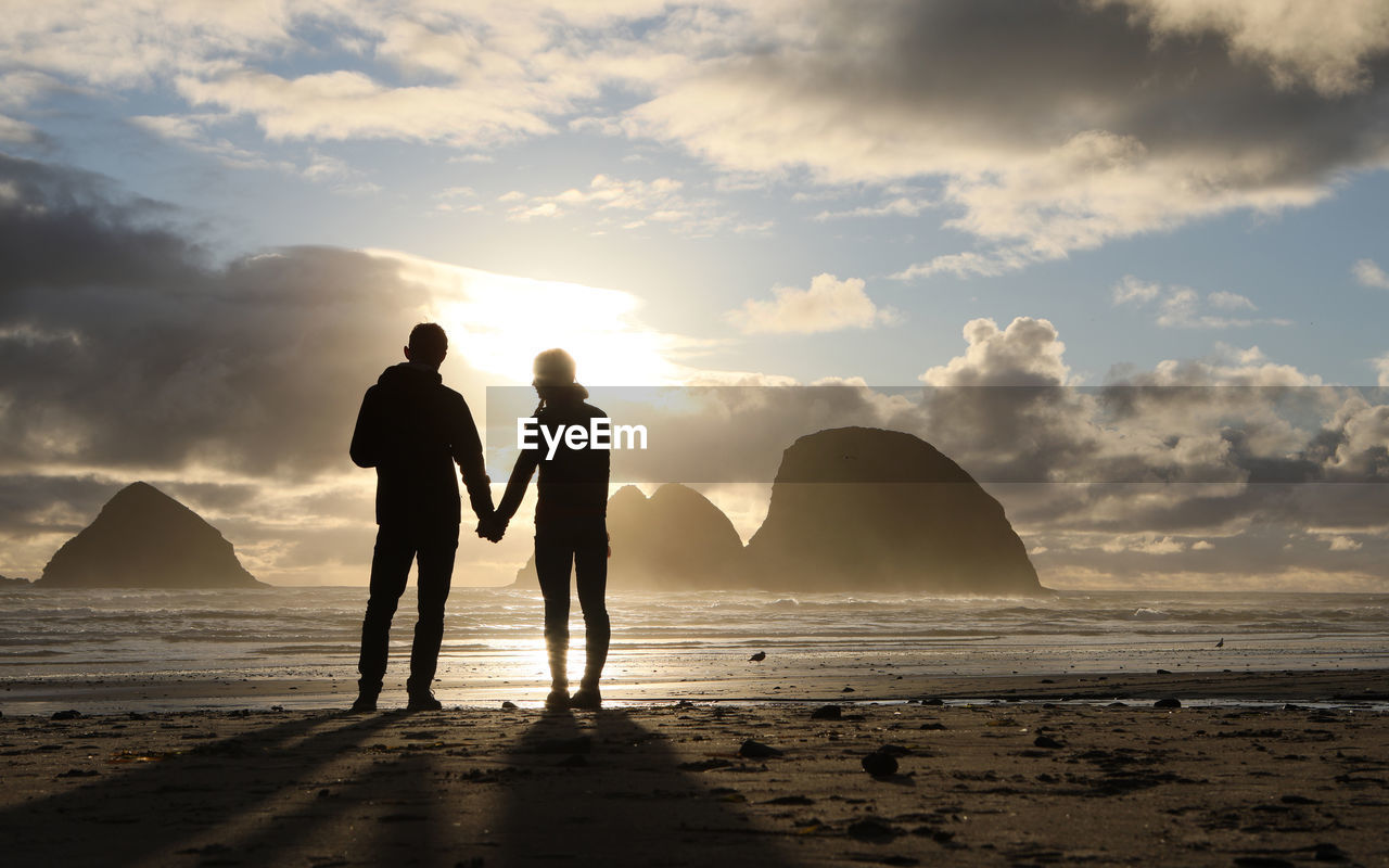 Couple standing on beach against sky during sunset