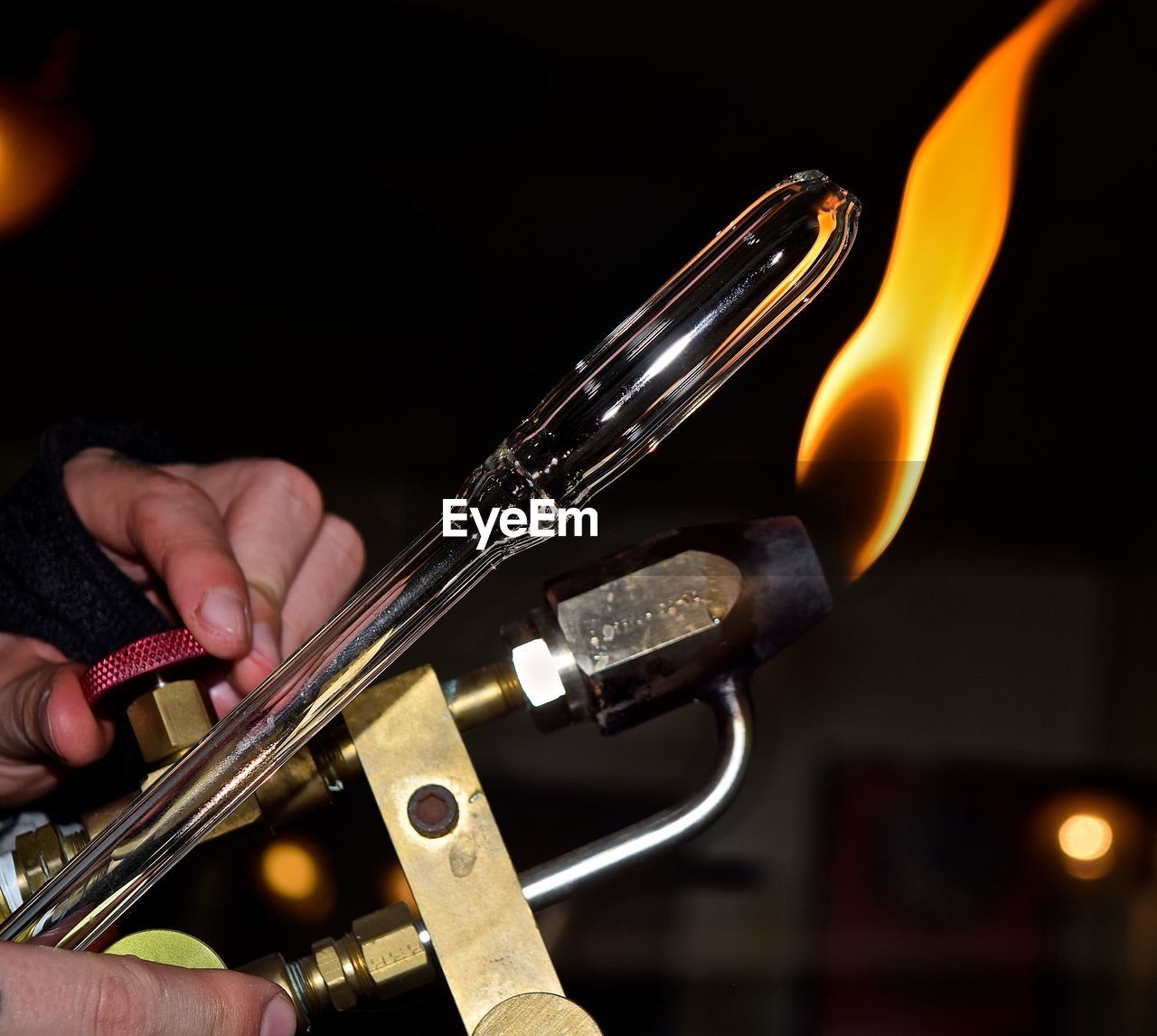 Cropped young woman holding flaming torch and glass in workshop