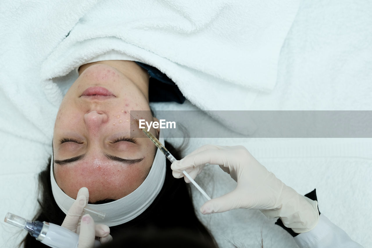 Cosmetologist applying face serum, preparing skin for microneedling