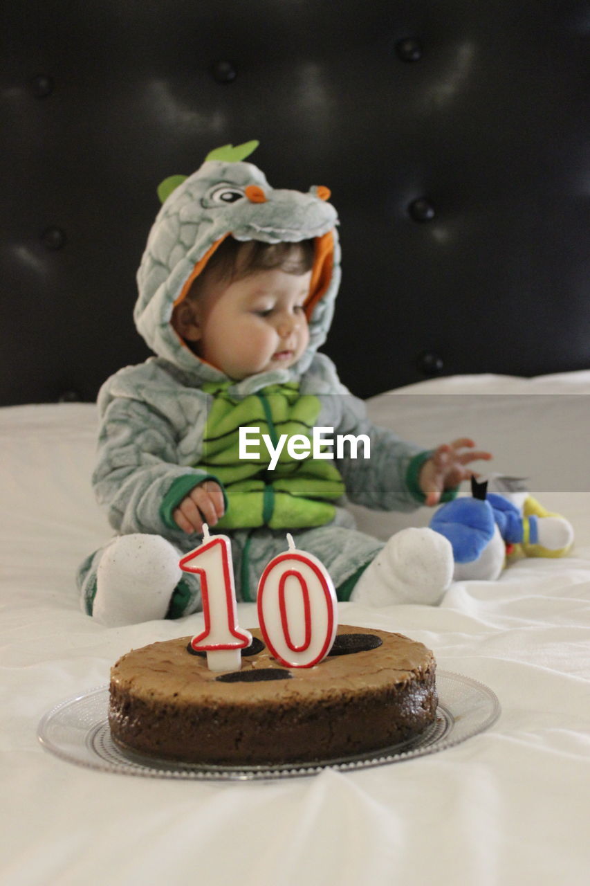Cute baby sitting by birthday cake on bed